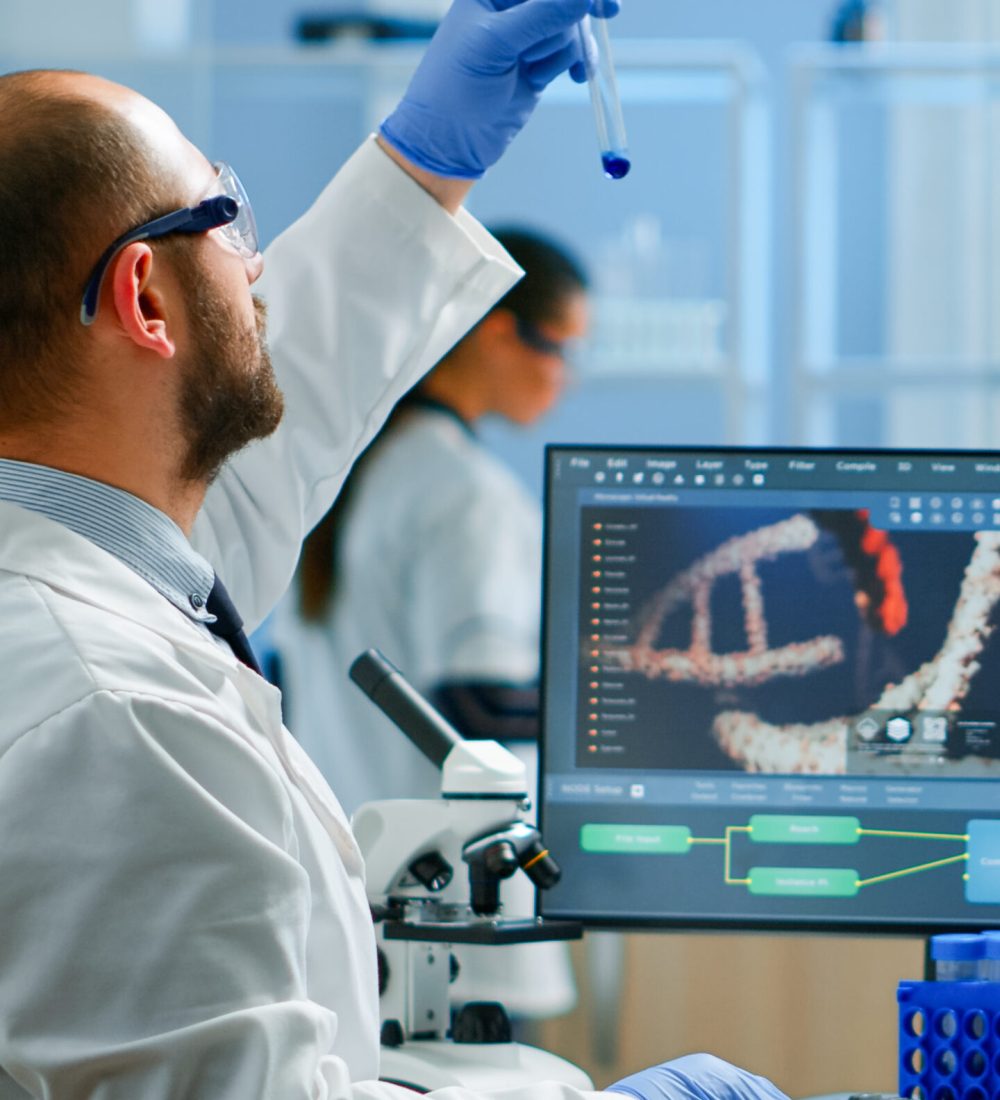Medical scientist working with DNA scan image in modern equipped laboratory holding test tube with sample. Team examining vaccine evolution using high tech and chemistry tools for vaccine development